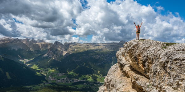 A person stands on the top of a rock with arms raised.