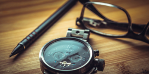 A pen, a pair of glasses and a watch sit on a table.