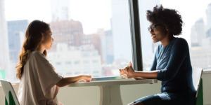 Two women sitting at a table in-front of a window having a conversation