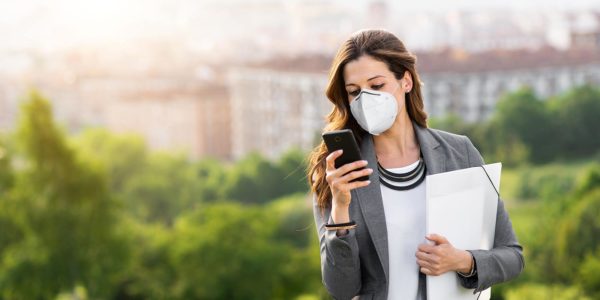A women wearing a mask holding a folder and checking here cell phone