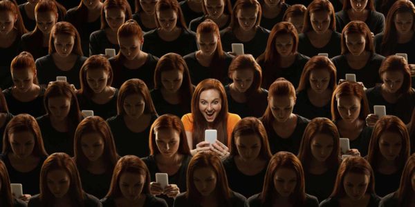 A large group of women all looking at their phones, with a spotlight on one in the middle.