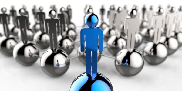 A group of silver metal figures of humans standing on metal balls, with the one in front colored blue.