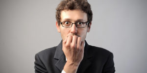 A man in a suit holding is hand up to his mouth in fear