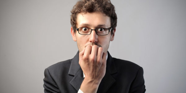 A man in a suit holding is hand up to his mouth in fear