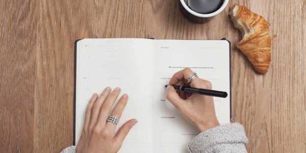 Planning_Out Woman writes in her planner with her breakfast on the table