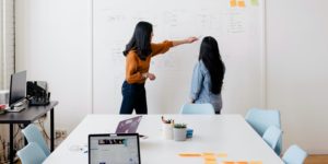 Two people standing in front of a white board with post-it notes and drawings on the board.