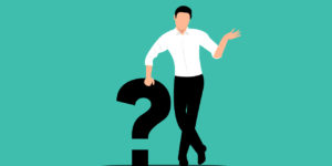 A person in a shirt and tie leaning on a black question mark.