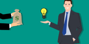 A person in a suit and tie holding a lightbulb receiving a bag of money from another person.