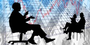 Silhouettes of two people having a meeting in front of a large graph with a red line moving up and down.