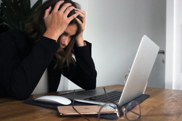 Frustrated_Woman A woman in a black long sleeve sits in front of her laptop with her head in her hands