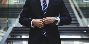 A man standing at the bottom of the stairs, adjusts his blue suit
