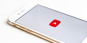 A white iPhone sits on a table while loading the Youtube app.