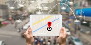 A person holds a tablet containing a map with a blurry city background and white pinpoints