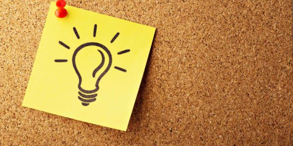 Thinking_about_Design A yellow sticky note pinned to a corkboard with a lightbulb drawn on it.