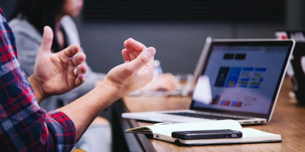 Two people sit at a table and have a discussion with open laptops in front of them.