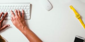 A person types on a keyboard with a yellow watch to their left.
