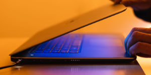 Hands open up a laptop with colorful neon lights surrounding it.