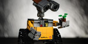 A yellow Wall-e holds and looks at a plant in his hand.