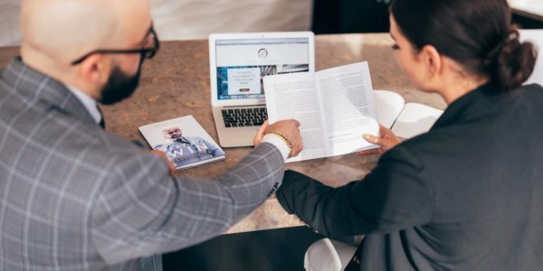 Two people in suits discuss plans sitting in front of a laptop.