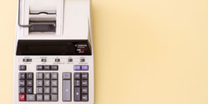 An old cash register on top of a pale yellow table.