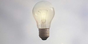 An outstretched hand with palm facing up towards a lit lightbulb. 