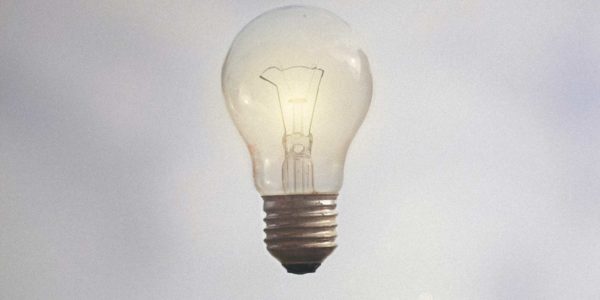 An outstretched hand with palm facing up towards a lit lightbulb.