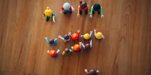 Four larger lego people stand in a line in front of ten smaller lego people.