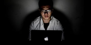 A person sits behind a laptop with the lights off.