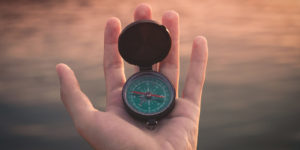 An outstretched hand holds a compass that points east.