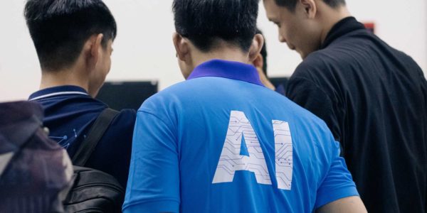 AI_Adopter Three men stand together, looking down at something, with one man in a blue AI polo.