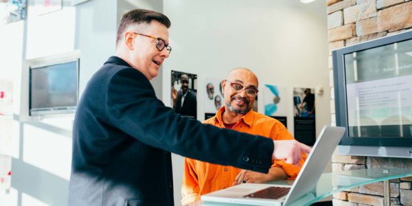 A man in a business suit points to a screen while talking to another man.