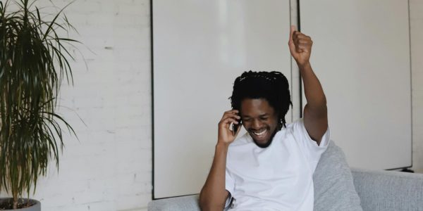 Man_Cheers A man sits on the couch on the phone with a happy expression and fist in the air.