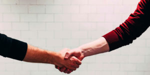Two people shaking hands near white painted wall.