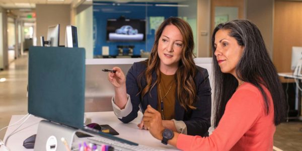 Two women sitting at a table looking at a computer screen.
