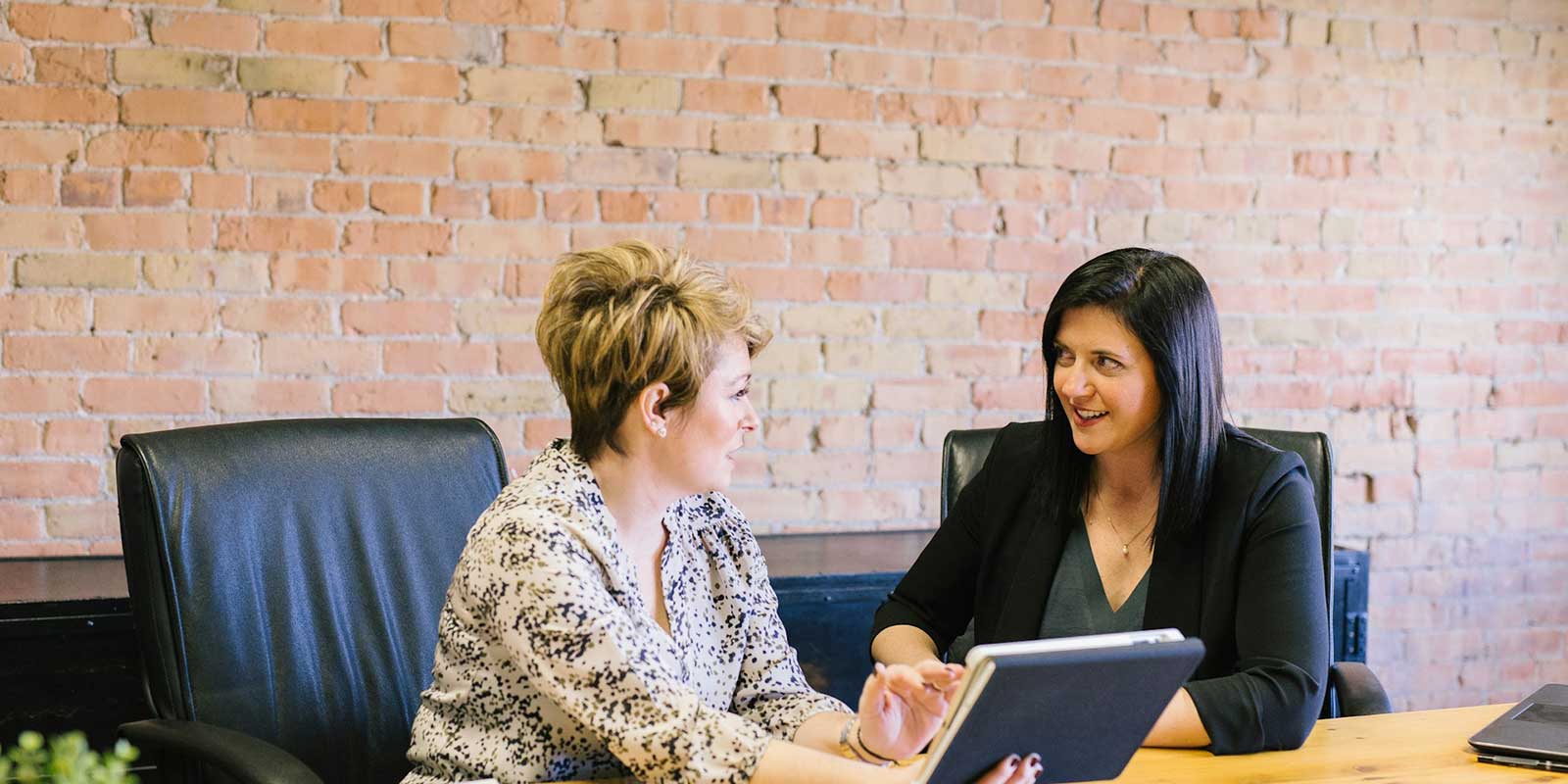 Two women sitting in chairs at a table conversing.