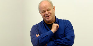Martin Seligman, American psychologist, speaking on stage holding notes and a clicker during a presentation
