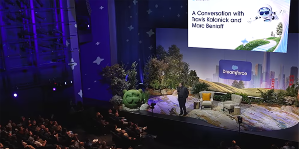 Dreamforce_Tech_Conference_Stage_Conversation_With_Travis_Kalanick_And_Marc_Benioff Speaker on stage at Dreamforce conference with audience watching a presentation titled “A Conversation with Travis Kalanick and Marc Benioff”